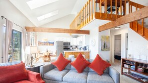 Ein geräumiger Wohnbereich mit einem grauen Sofa, roten Kissen und einer Holztreppe.