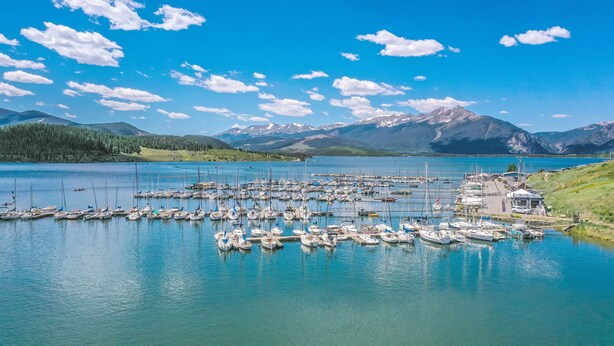 Un port de plaisance où sont amarrés des bateaux, entouré de montagnes et surplombé par un ciel bleu clair.