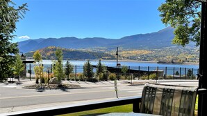 Vue depuis un balcon, avec une table en verre, donnant sur un lac et des montagnes.
