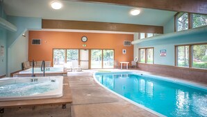Una piscina interior con un jacuzzi, sillones de descanso y un reloj en la pared.
