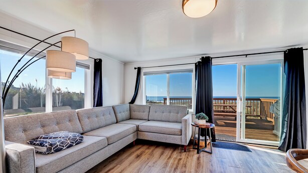 Uma sala de estar moderna com um sofá seccional, uma mesinha e vista para um deck de madeira através de grandes janelas.