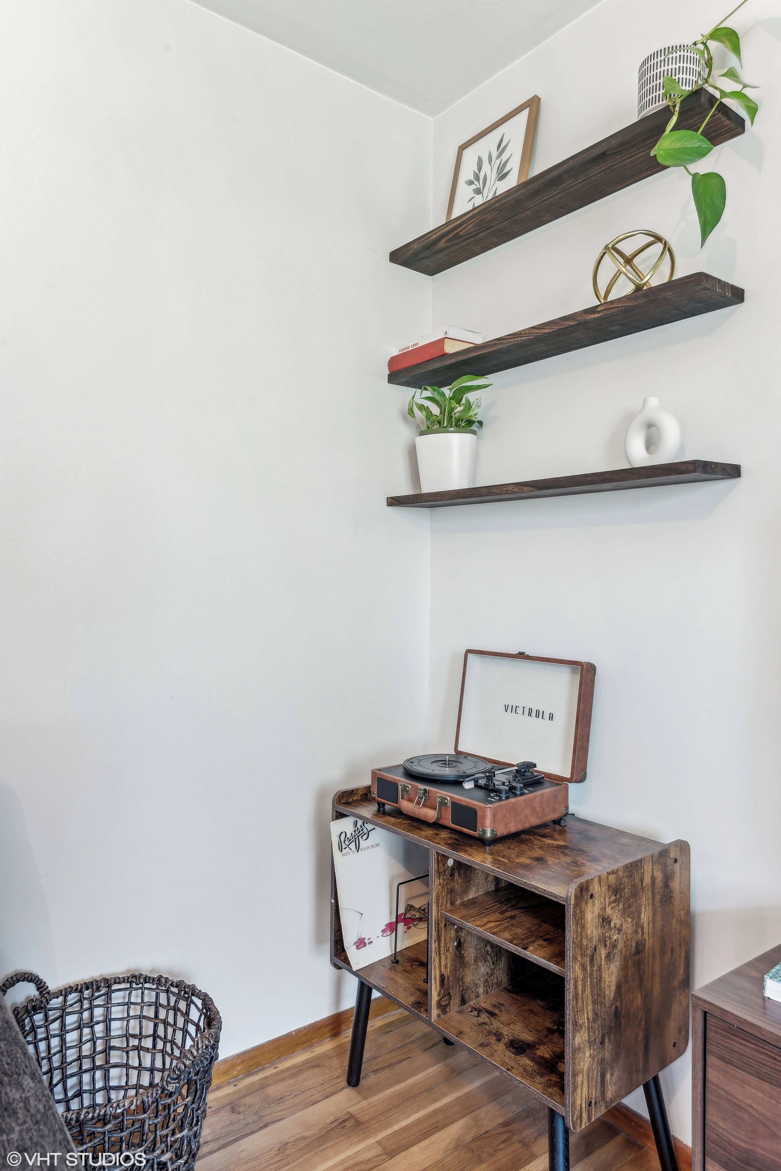 A corner with a wooden desk, a vintage record player, and a plant on a shelf.