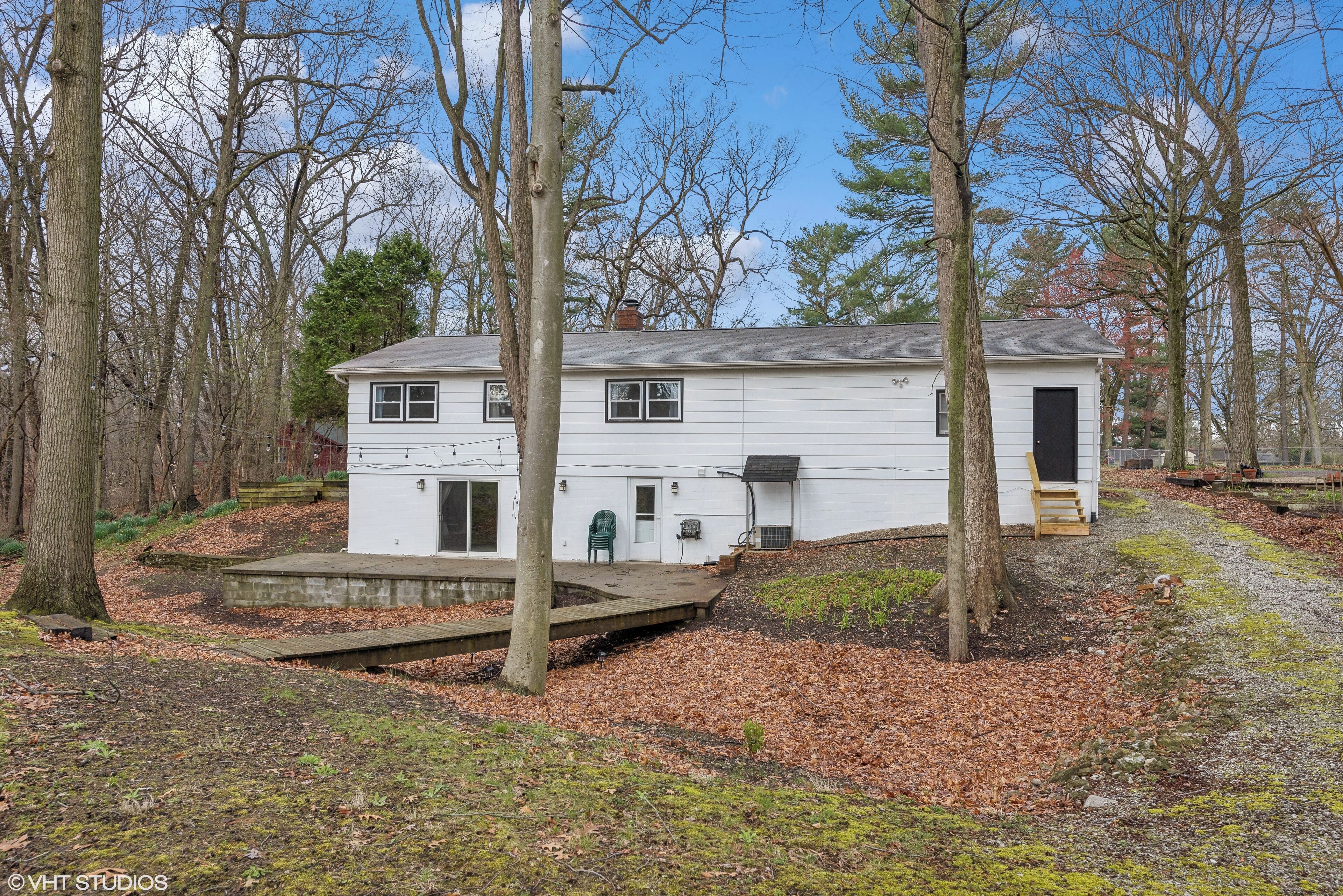 A white two-story house with a front porch, surrounded by trees and a small deck.
