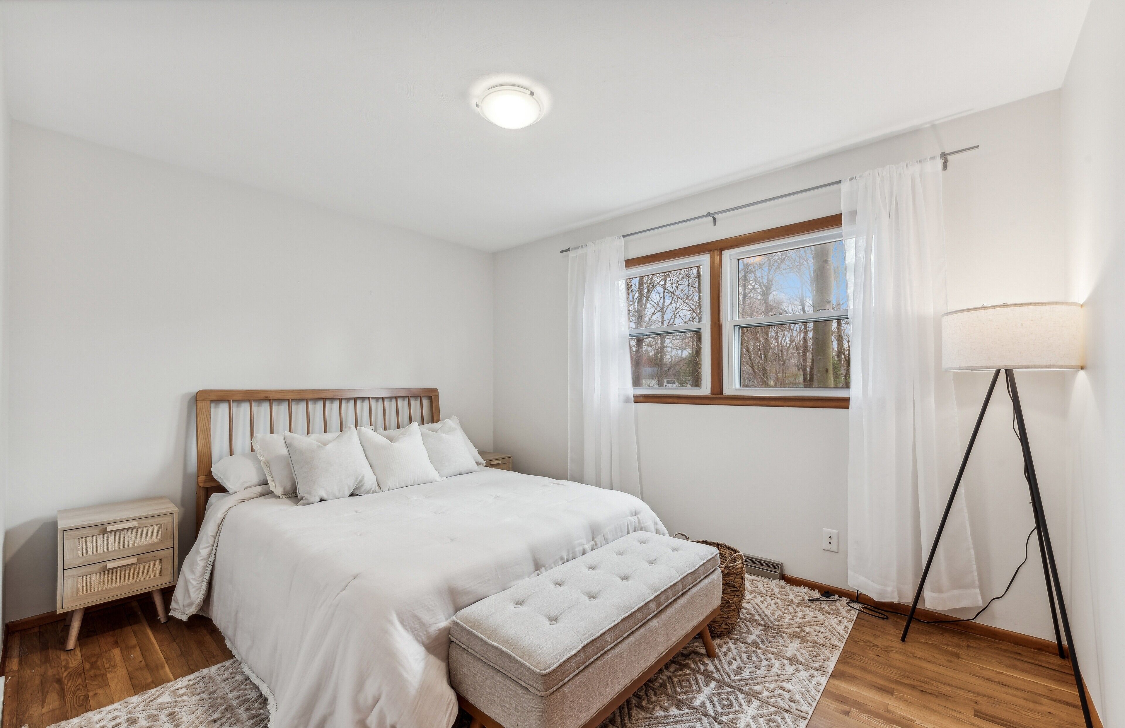 A bedroom with a bed, bedside tables, a window with curtains, a standing lamp, and a patterned rug.