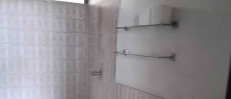 A small bathroom with a toilet, sink, and shower. There are shelves above the sink and a window above the shower.