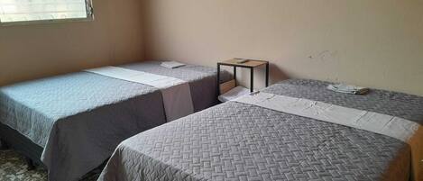 A room with two single beds, a small table, and a window with blinds.