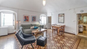 Een woonkamer met een bank, een salontafel, een eettafel met stoelen en een vloer met een patroon.