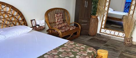 A bedroom with a bed, a wicker chair, a wardrobe, and a mirror reflecting a bed.