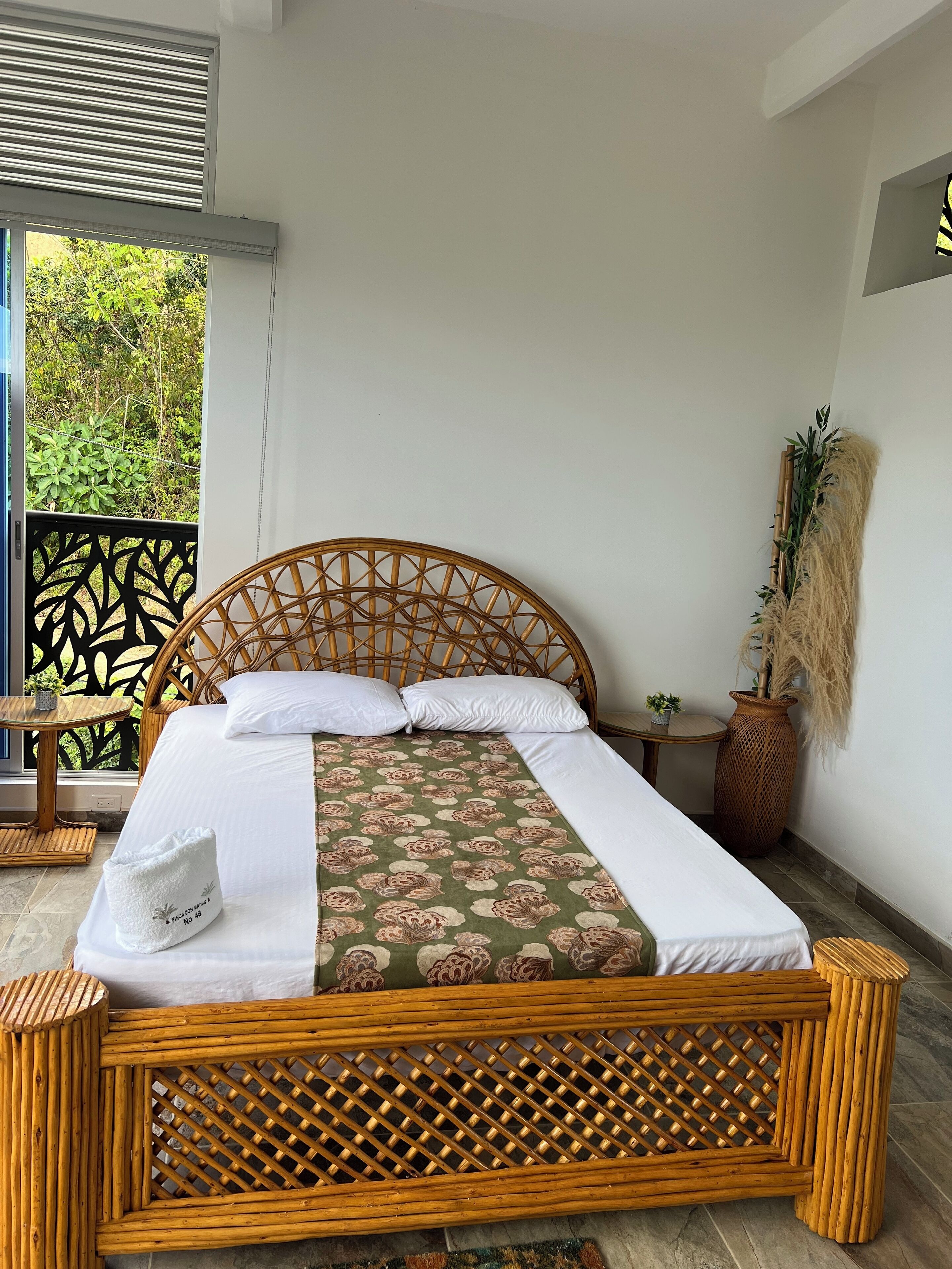 A bed with a woven headboard, white bedding, and a floral-patterned bedspread.