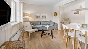 Een moderne woonkamer met een grijze bank, een ronde salontafel en een eethoek met witte stoelen en een tafel.