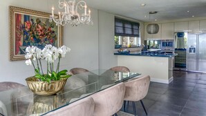Una cocina moderna con electrodomésticos de acero inoxidable, una mesa de comedor de vidrio y una araña.