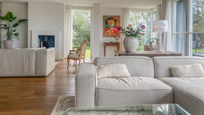 Una sala de estar moderna con un sofá gris, una mesa de centro de vidrio y un ventanal con vistas a zonas verdes.