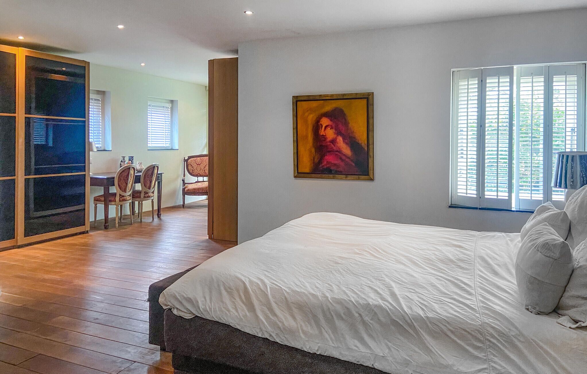 Un dormitorio con una cama grande, un cuadro en la pared y un rincón comedor al fondo.