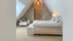 Un dormitorio con techo inclinado, cama, mesita de noche, silla y lámpara.