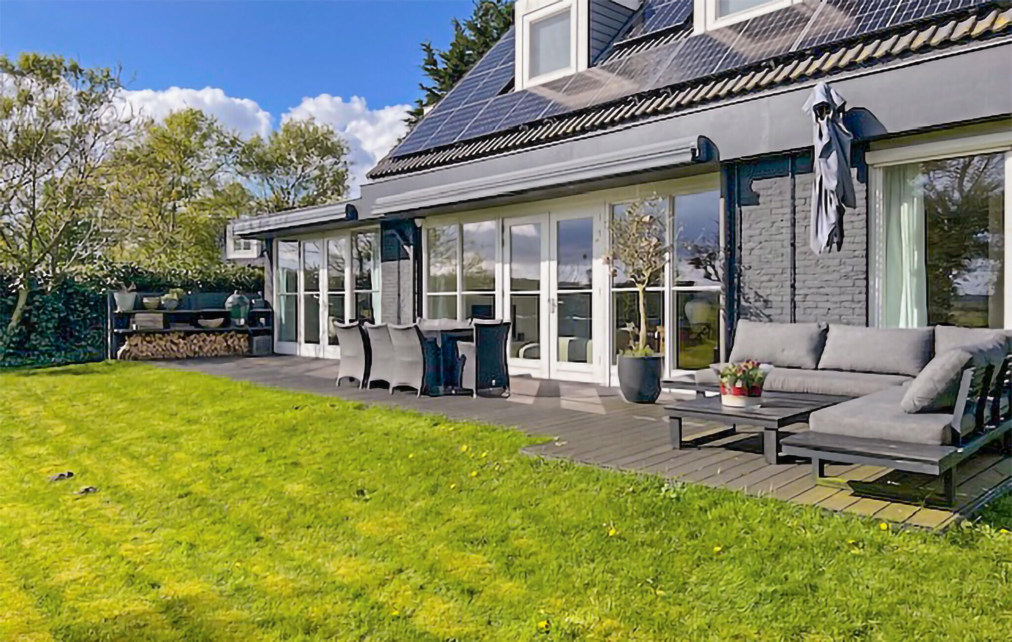 Ein modernes Haus mit einer großen Terrasse, einem Essbereich und einer Sitzgruppe inklusive Sofa und Tisch.
