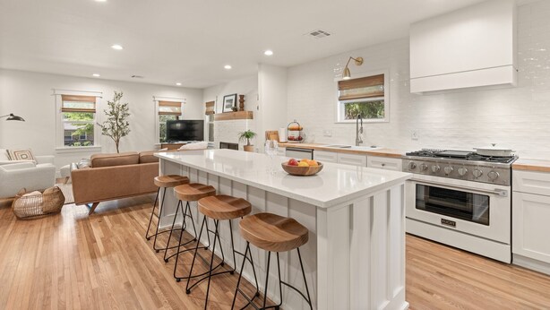 A modern kitchen with white cabinetry, a central island with stools, a built-in oven, and a large window providing natural light. - Luxury 3BD 2bath Near EXPO & TU (Tulsa)