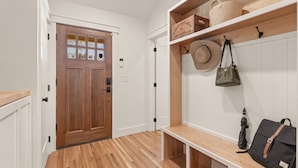 A hallway with a wooden door, white walls, a bench, and a shelf with bags and a hat. - Luxury 3BD 2bath Near EXPO & TU (Tulsa)