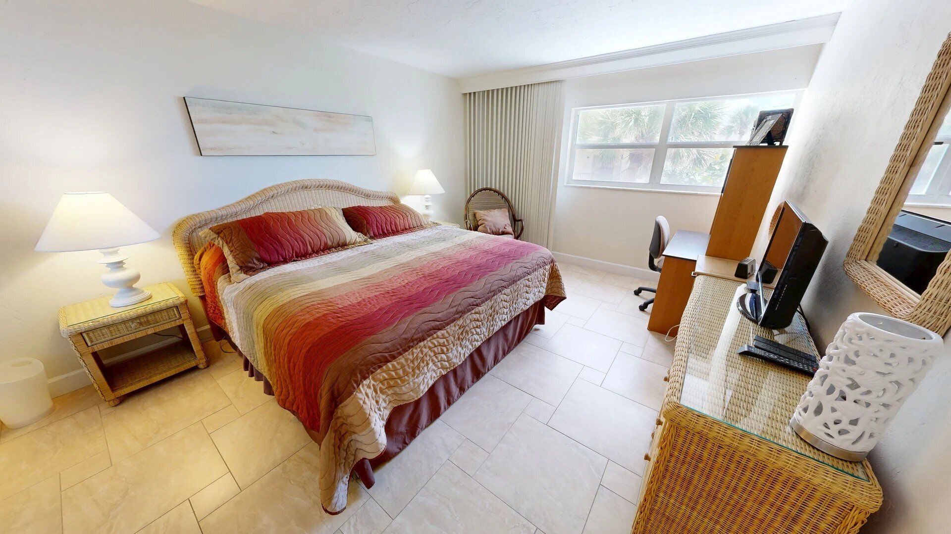A bedroom with a bed, bedside tables, a desk, a chair, a mirror, and a window with curtains.