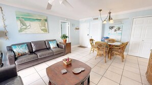 A living room with a dark leather sofa, a round wooden coffee table, and a dining area with wicker chairs and a glass table. - Crescent Arms Vacation Rentals 403 N Siesta Key Florida (Siesta Key)