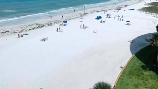 Une plage de sable blanc, avec une eau d’un bleu limpide et quelques parasols.