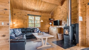 En mysig stuga med en lädersoffa, ett bord, en tv och en vedkamin.