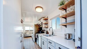 A modern kitchen with white cabinets, wooden shelves, and a built-in toaster. - Beachcomber: Beachfront Escape Unit #4 (Florence)