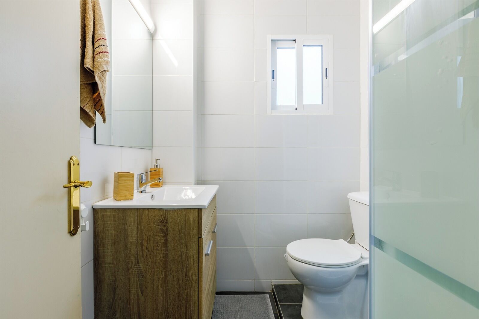 Une salle de bain avec un lavabo blanc, un meuble-lavabo en bois, des toilettes et une douche à parois de verre.