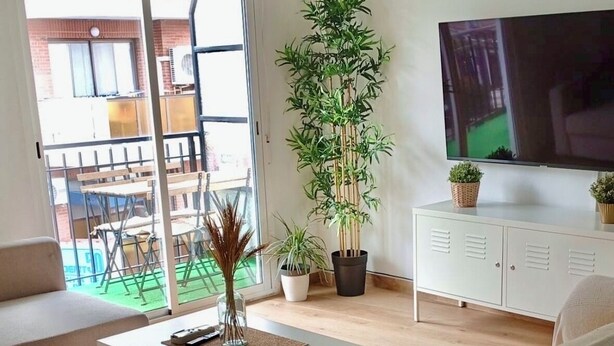 Una sala de estar moderna con sofá, una mesa de centro, televisor y un balcón con mobiliario exterior.