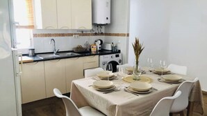 Un comedor con una mesa lista para cuatro personas, una cocina al fondo y un armario blanco sobre el fregadero.