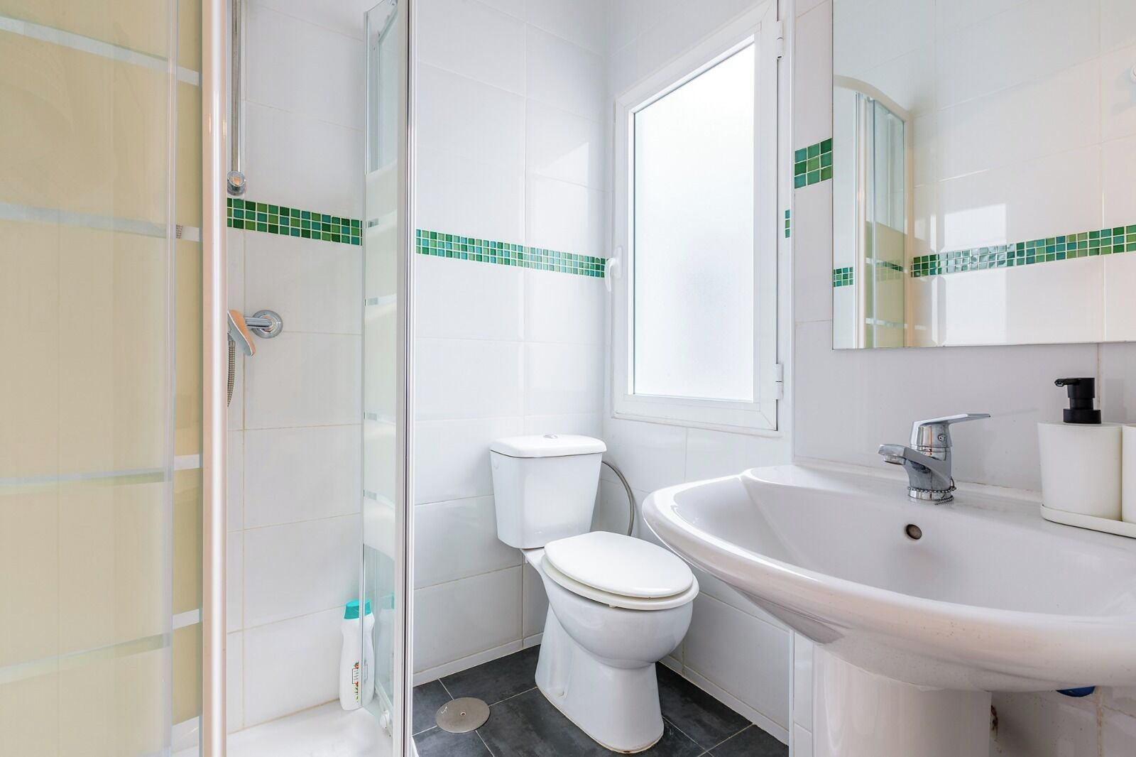 Un baño con cabina de ducha de vidrio, inodoro, lavabo y ventana.