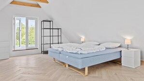 Quarto com cama, mesas de cabeceira, um estante e janela com vista para vegetação.