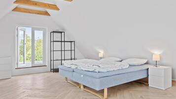 A bedroom with a bed, bedside tables, a shelf, and a window with a view of greenery.