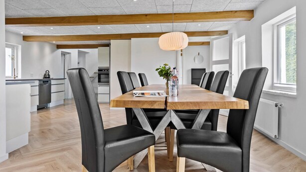 Uma área de refeições moderna com uma mesa de madeira, cadeiras de couro preto e uma luminária pendente.