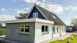 Uma casa moderna com telhado inclinado, uma pequena garagem anexa e um caminho de acesso pavimentado.