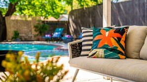 A poolside area with a sofa and lounge chairs, a pool, and a wooden fence in the background. - Country Pool House w/ Game Room, Fire Pit, Grill (North Richland Hills)