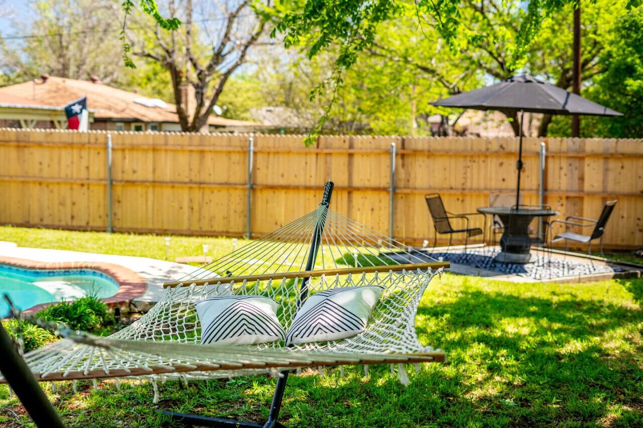 A hammock chair with pillows, a pool, and a patio area with chairs and an umbrella.