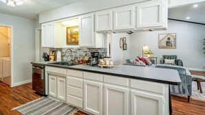 A kitchen with white cabinets, a black countertop, and a wooden floor. - Country Pool House w/ Game Room, Fire Pit, Grill (North Richland Hills)