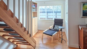 Una escalera con detalles de madera, una silla con cojín estampado, una mesita redonda pequeña y una estantería con varios libros.