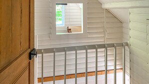 Una habitación con techo inclinado, un ventanal pequeño y barandilla blanca.