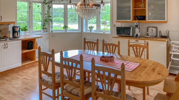 Una cocina con una mesa de madera, sillas, una araña y vistas al verdor exterior.