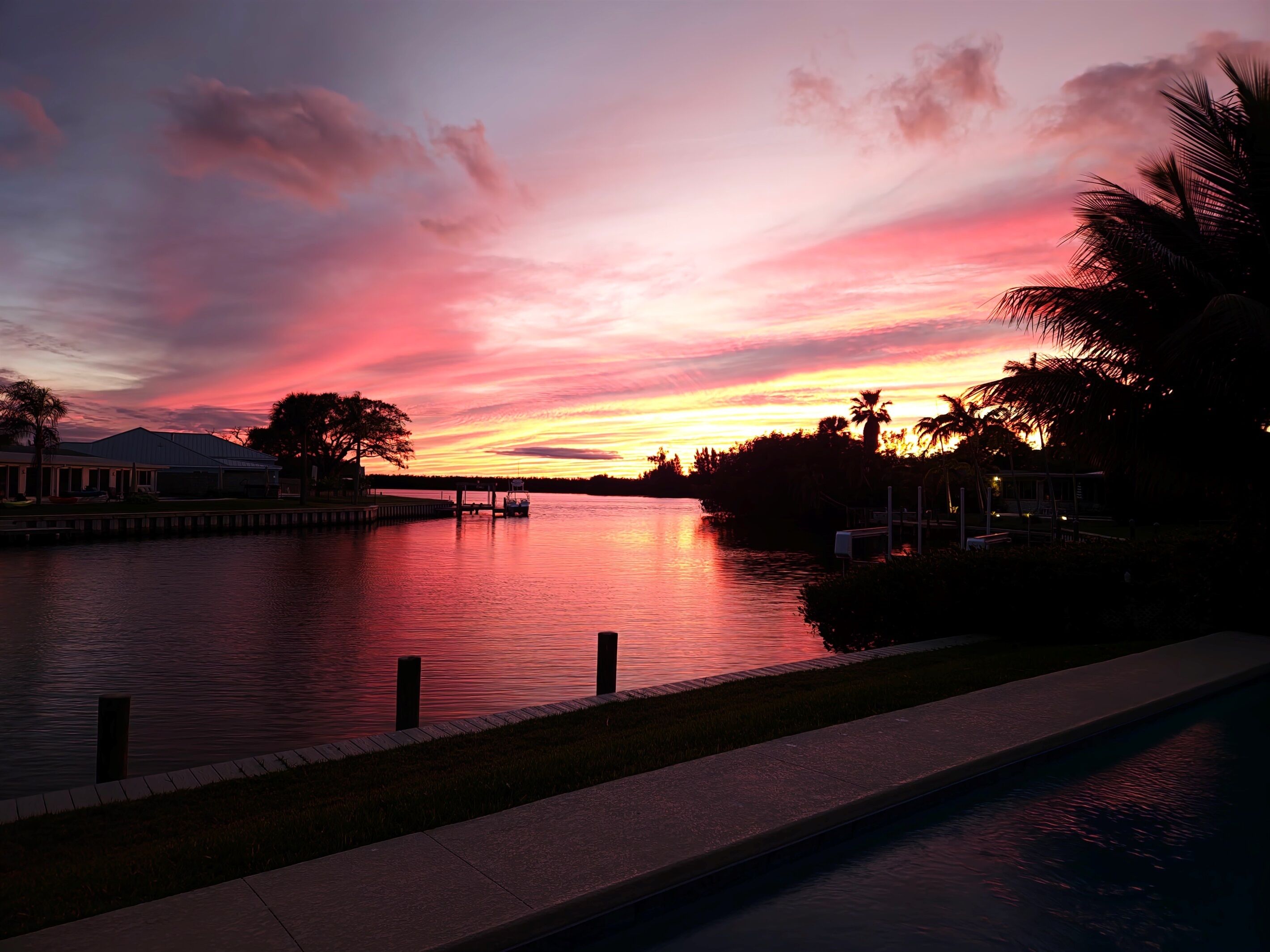 A waterfront view with a sunset, calm water, and a dock.