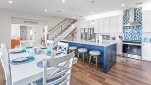A modern kitchen with a central island, stainless steel appliances, and a blue backsplash. - Canal-Front Home with Heated Pool (Cocoa Beach)