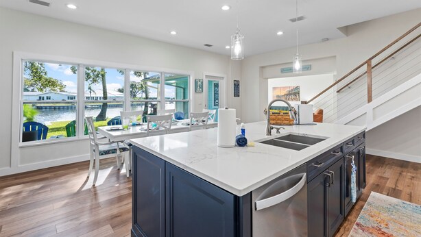 A modern kitchen with a large island, white countertops, and dark cabinetry. There is a view of a river and greenery outside the windows. - Canal-Front Home with Heated Pool (Cocoa Beach)