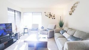 Ein modernes Wohnzimmer mit Flachbildfernseher, einer Couch, einem Couchtisch und einem Sessel.
