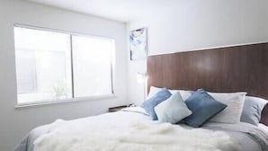 Ein Schlafzimmer mit einem großen Fenster, einem hölzernen Kopfende und einer flauschigen weißen Decke.