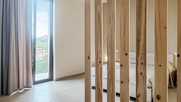 A room with a large sliding glass door leading to a balcony, a bed, and a wooden partition. - Stunning apartment in Patti with WiFi (Patti)