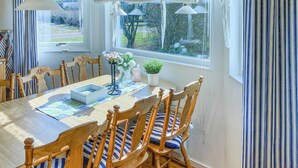 Une salle à manger avec une table en bois, des chaises à rayures et une vue sur le jardin grâce à de grandes fenêtres.