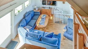 Un vaste espace de vie comprenant un grand canapé bleu, une table basse en bois et un escalier menant à un niveau supérieur.