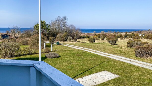 Une propriété située sur la côte, offrant une vue dégagée sur la mer, avec une pelouse verdoyante et un chemin menant à un petit bâtiment.
