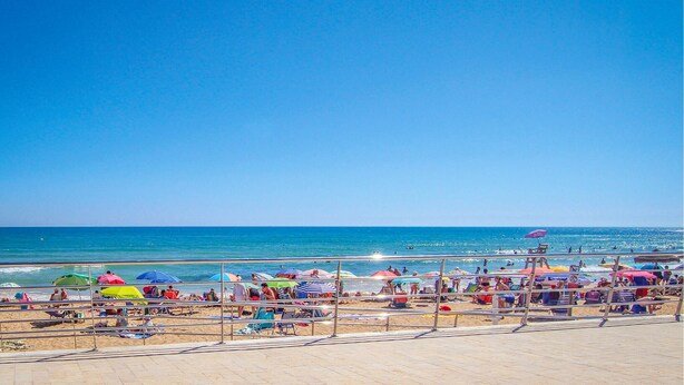 A beach with a clear sky, people relaxing on the sand, and colorful umbrellas. - 2 bedroom lovely apartment in Miramar (Miramar)
